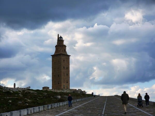 Gente paseando junto a la torre de Hércules por el paseo marítimo de A Coruña